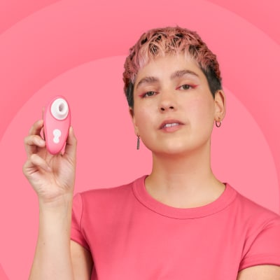 ピンクの背景の前で、ピンク色の吸引タイプのおもちゃを手に持つ女性